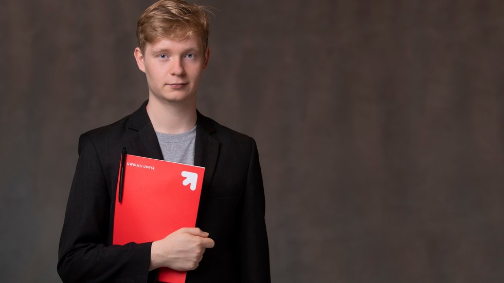 Student UniLodz trzymający czerwoną teczkę na dokumenty.