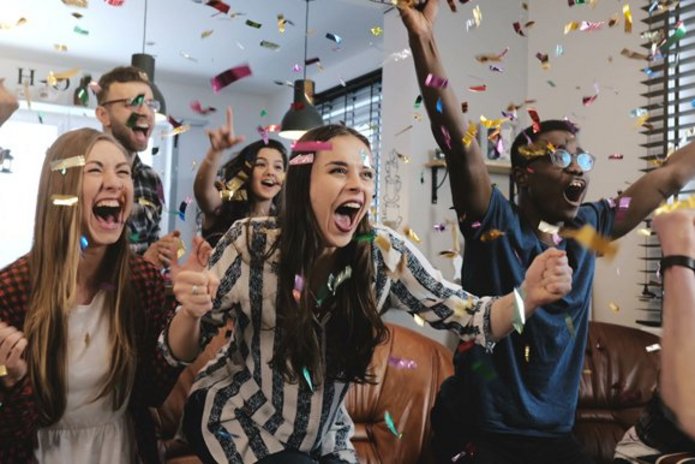 Zdjęcie przedstawiające grupę cieszących się młodych ludzi w chmurze confetti.