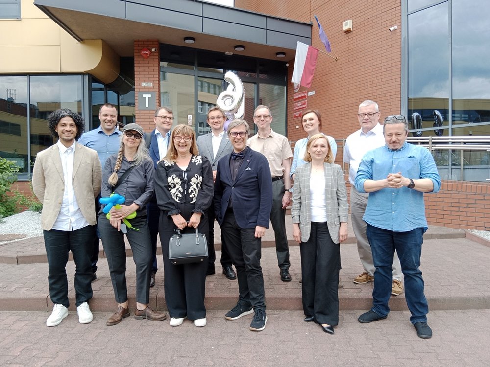 grupa uśmiechniętych ludzi w eleganckich strojach stojących przed budynkiem uniwersytetu