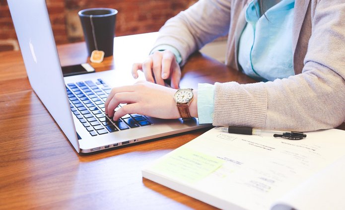 Widok biurka, osoba pisze na laptopie, obok notes. Nie widać twarzy