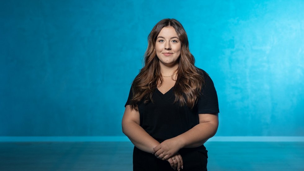 Dziewczyna z rozpuszczonymi włosami stoi na tle niebieskiej ściany.