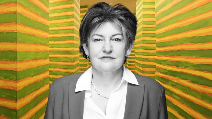 Prof. Aneta Pawłowska on the background of a painting installation by Leon Tarasewicz. This work consists of two parallel rows of 24 identical columns. They are located in a narrow, straight corridor that connects two different parts of the exhibition. The columns are painted with horizontal green, yellow and orange stripes.