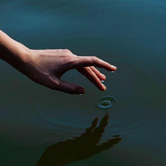 Zdjęcie rzeki i dłoni z zanurzanym w wodzie palcem 