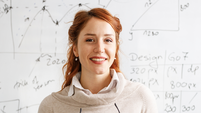 a portrait of a smiling woman against a white board with black lettering 
