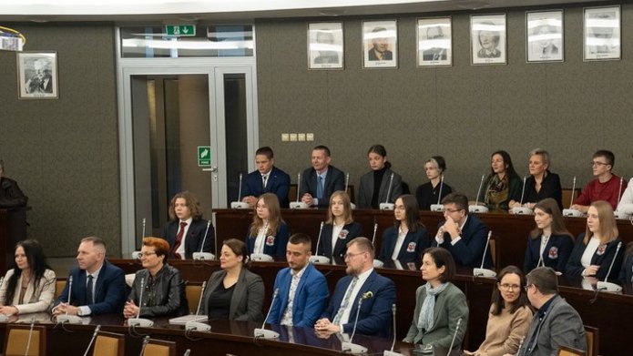 Grupa uczniów i wykładowców w auli akademickiej.