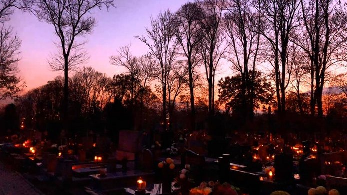 widok cmentarza o zmierzchu, z płonącymi na grobach zniczami