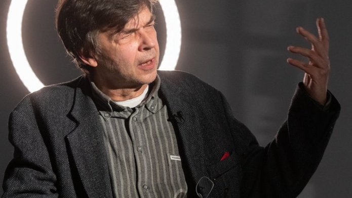 Autor tłumaczenia siedzi w sali i opowiada, gestykulując. 