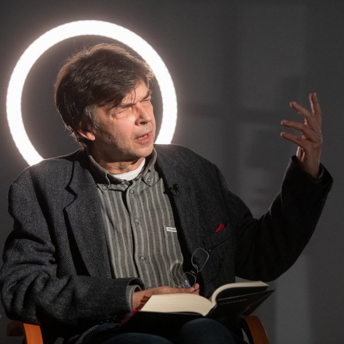 Autor tłumaczenia siedzi w sali i opowiada, gestykulując. 