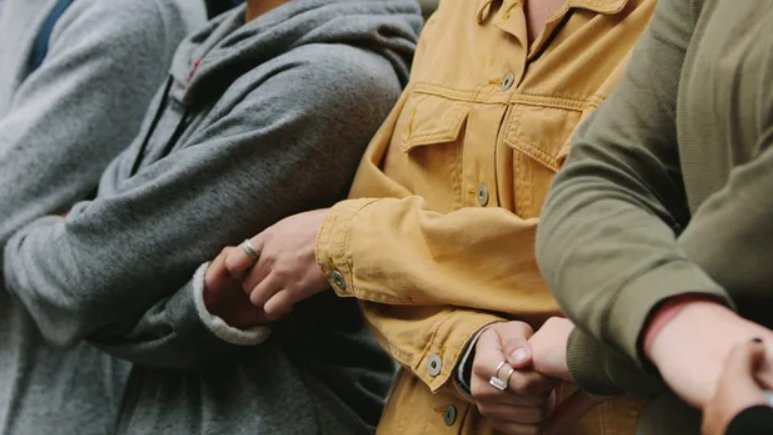 Zdjęcie przedstawia sylwetki osób, które trzymają się nawzajem za ręce 