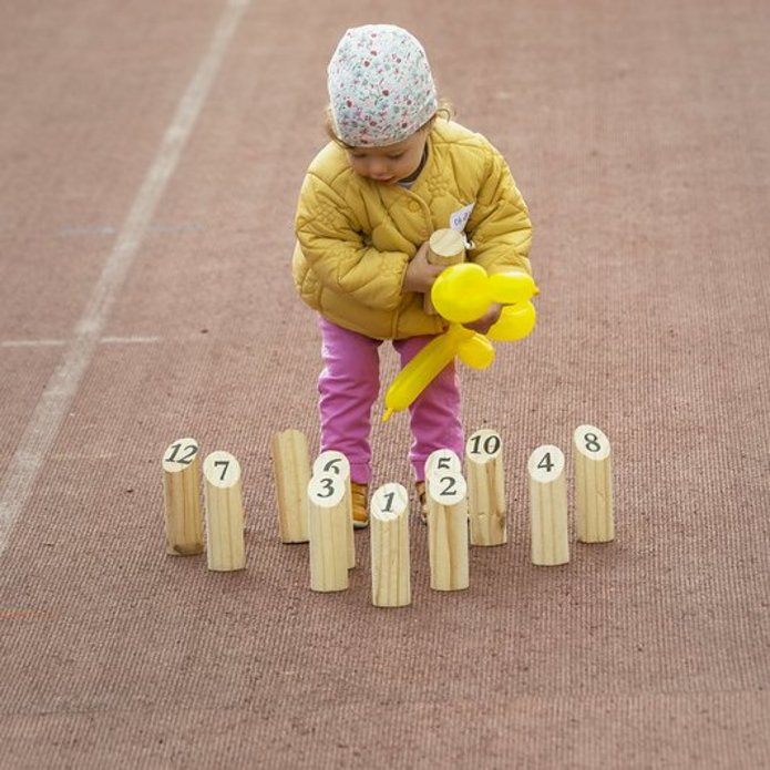 Dziecko z żółtym balonem, stojące wśród drewnianych zabawek