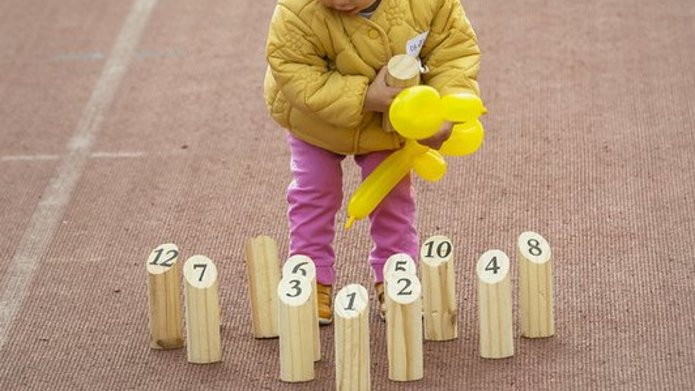 A child with a yellow balloon, standing among wooden toys
