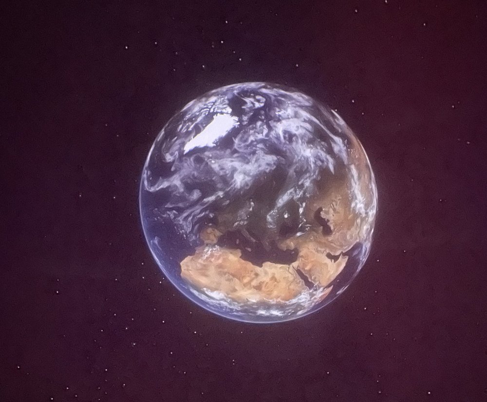 Zdjęcie przedstawia planetę Ziemię na tle ciemnego, fioletowo-granatowego nieba.