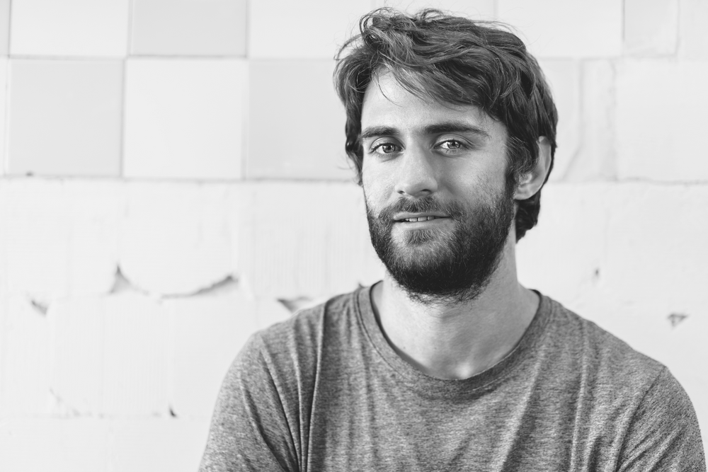 a decorative element: a black and white photo of a smiling young man with a beard looking straight into the camera