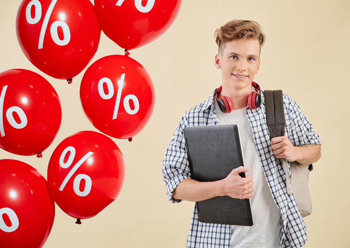 Na zdjęciu widać mężczyznę. Stoi przodem do nas, w prawej dłoni trzyma dokumenty i laptop, przez lewe ramię przewieszony ma plecak. Po jego prawej stronie widać balony w kolorze czerwonym, które mają biały symbol procent nadrukowany na powierzchni. Balony unoszą się w powietrzu.