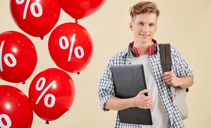 Na zdjęciu widać mężczyznę. Stoi przodem do nas, w prawej dłoni trzyma dokumenty i laptop, przez lewe ramię przewieszony ma plecak. Po jego prawej stronie widać balony w kolorze czerwonym, które mają biały symbol procent nadrukowany na powierzchni. Balony unoszą się w powietrzu.