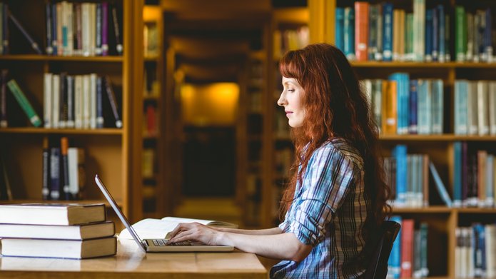 kolorowe zdjęcie przedstawiające studentkę pracującą w bibliotece; zdjęcie promuje artykuł poświęcony nowym zasadom konkursu Studenckie Granty Badawcze 2023