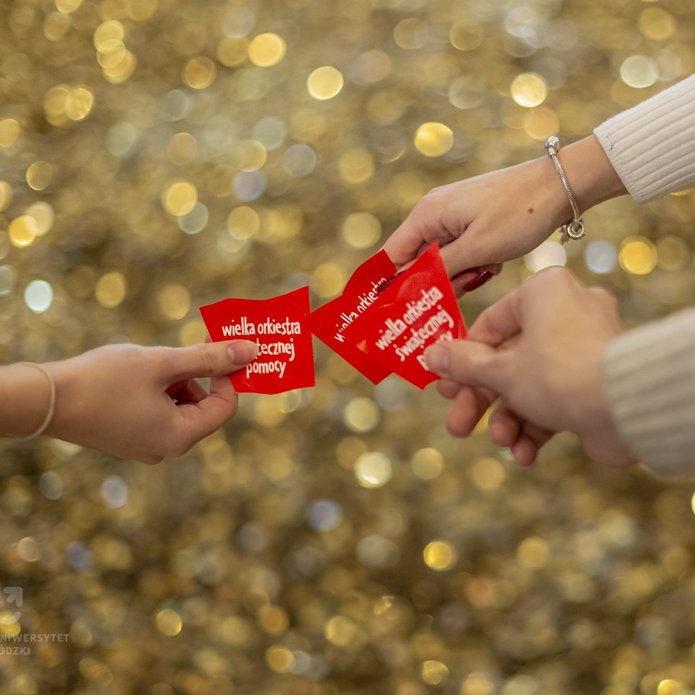 3 hands holding red hearts with the inscription "Great Orchestra of Christmas Charity" on a background of gold coins