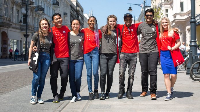 A group of young people of all colours are standing on Piotrkowska Street in Lodz. They are smiling and wearing University of Lodz T-shirts.