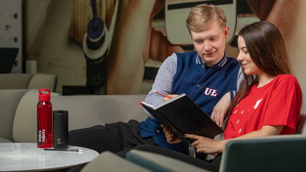Student i studentka siedzą na kanapie i patrzą w notatnik