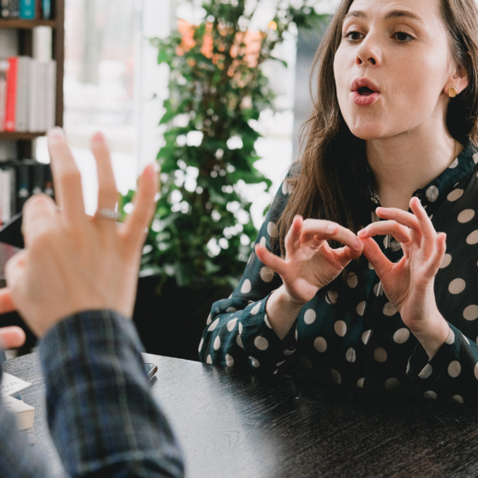 Dwie kobiety siedzące naprzeciwko siebie, uczą się języka migowego