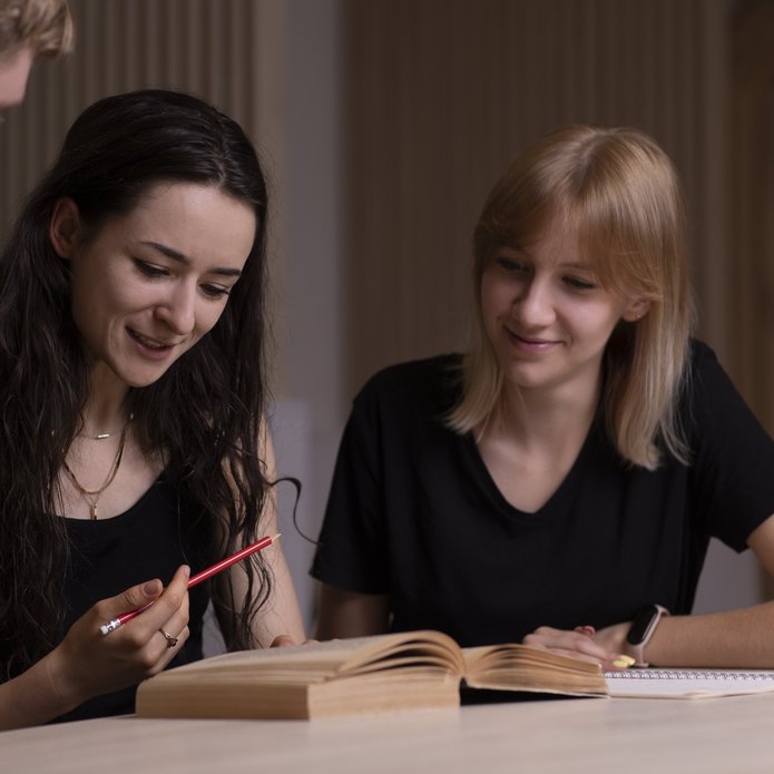 2 studentki rozmawiające i patrzące w książkę