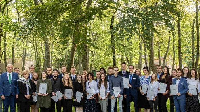 A group photo of honoured students and the University of Lodz authorities with trees in the background