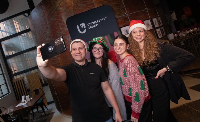 Ambasadorzy UŁ w świątecznych strojach robią sobie zdjęcie na tle ścianki UŁ
