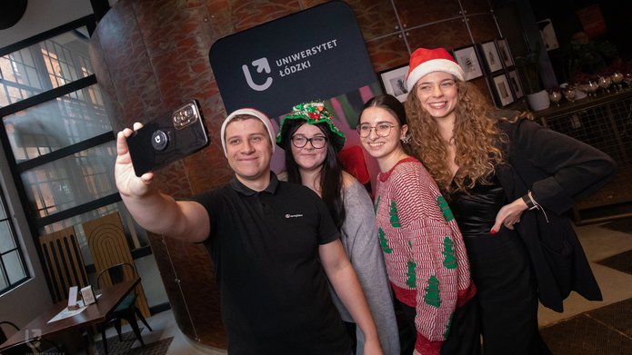 Ambasadorzy UŁ w świątecznych strojach robią sobie zdjęcie na tle ścianki UŁ