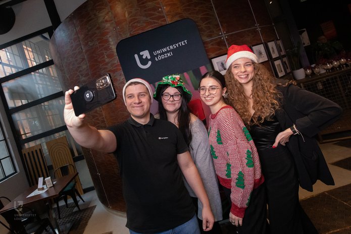 Ambasadorzy UŁ w świątecznych strojach robią sobie zdjęcie na tle ścianki UŁ