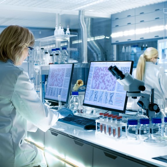 Female and Male Scientists Working on their Computers In Big Modern Laboratory. Various Shelves with Beakers, Chemicals and Different Technical Equipment is Visible. Element dekoracyjny