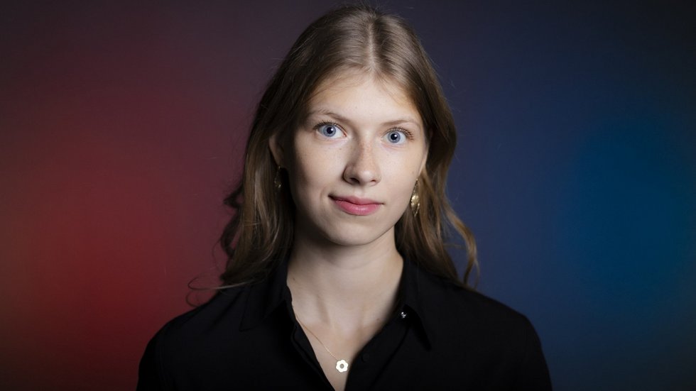 Blond dziewczyna z długimi włosami na tle fioletowo granatowej ściany