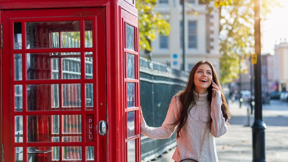 photo of a smiling young woman standing next to a London phone booth