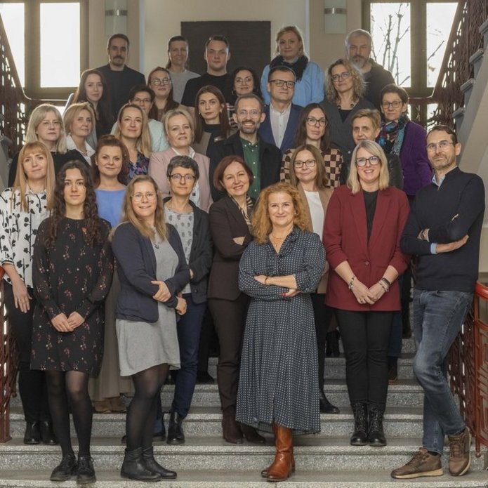 Duża grupa ludzi, kobiet i mężczyzn, stojących na schodach na klatce schodowej Uniwersytetu Łódzkiego.