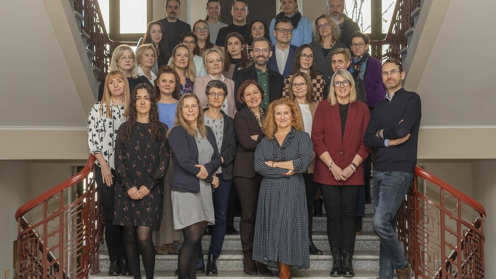 Duża grupa ludzi, kobiet i mężczyzn, stojących na schodach na klatce schodowej Uniwersytetu Łódzkiego.