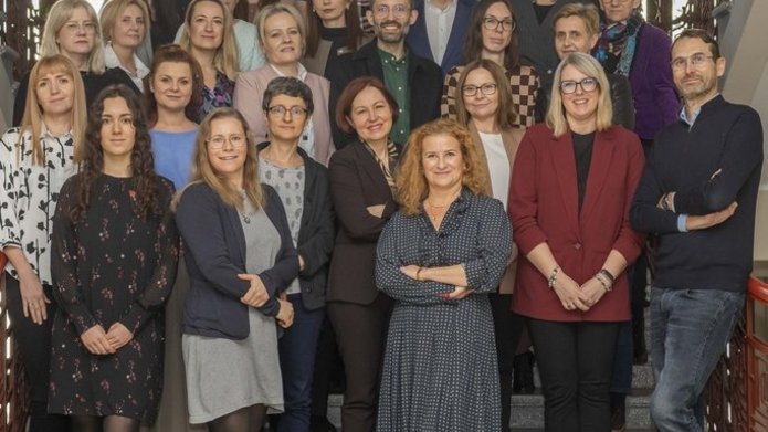 Duża grupa ludzi, kobiet i mężczyzn, stojących na schodach na klatce schodowej Uniwersytetu Łódzkiego.