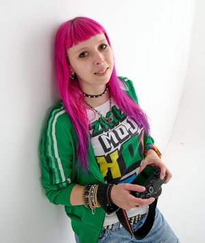 na zdjęciu autorka - dziewczyna o różowych włosach, z piercingiem na twarzy, trzyma aparat fotograficzny w ręce z aparatem fotograficznym w ręc