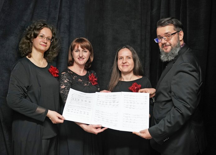 Trzy pianistki i kompozytor prezentują kartkę z fragmentem utworu