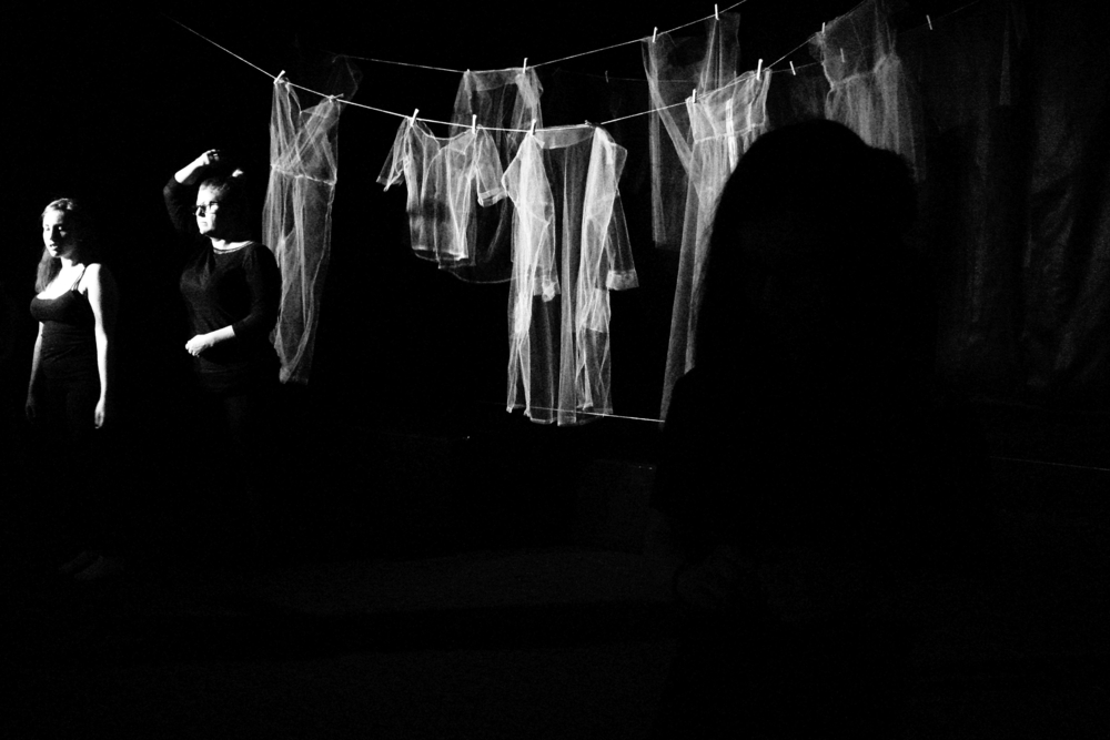 A black-and-white contrast photo from the performance, two women of different ages, clothes hanging behind them