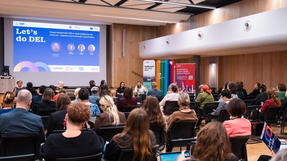 A group photo; in the background, the conference graphic featuring text and photos of the participants