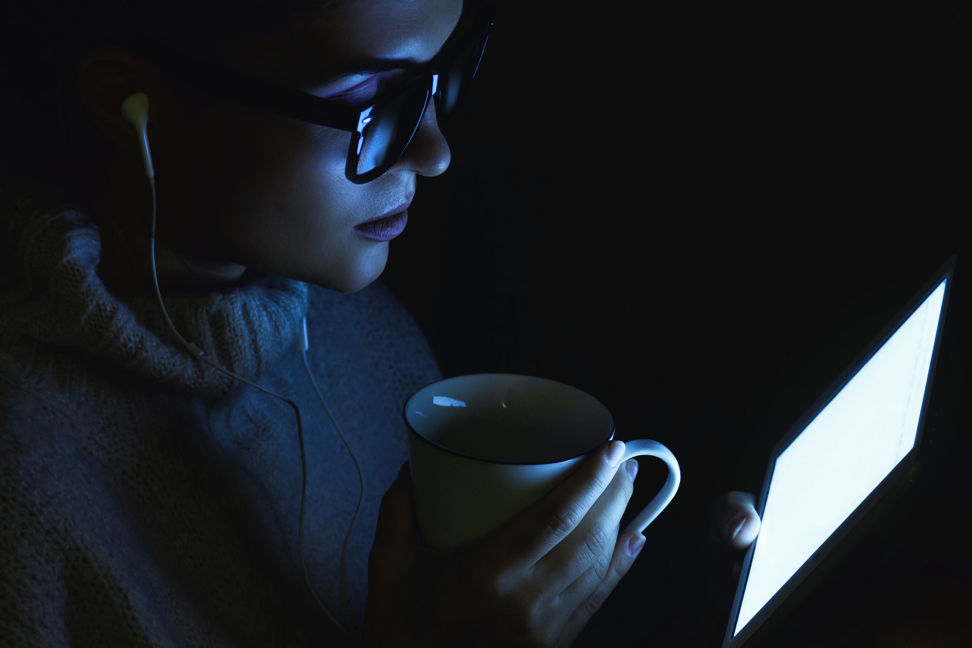 Młoda kobieta siedząca w ciemności przed ekranem tabletu