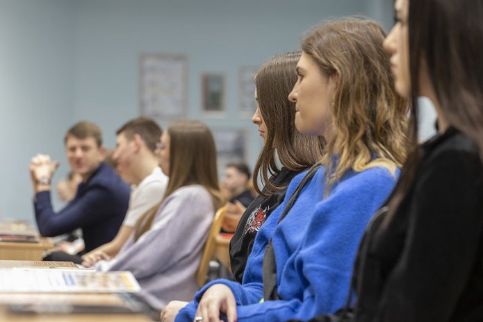 kolorowe zdjęcie przedstawiające z profilu grupę studentów siedzących w ławkach