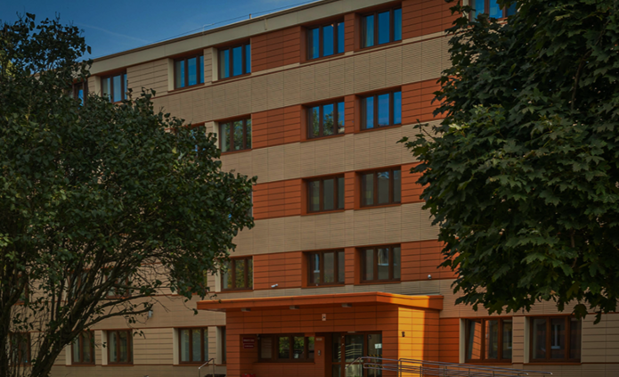 The photo shows a University of Lodz dormitory building surrounded by greenery. A large tree is in the foreground, with the dormitory entrance behind it. On the left side of the graphic is a white inscription: "Find your place. Recruitment for the University of Lodz dormitories." In the upper right corner, a red arrow points up and to the right.
