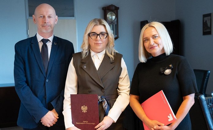 Trzy osoby trzymające teczki z podpisanym porozumieniem.