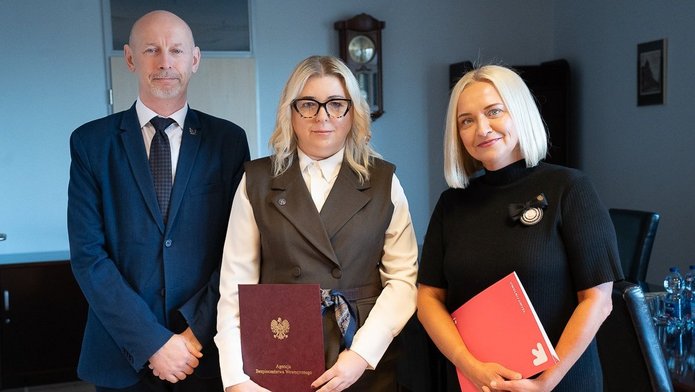 Trzy osoby trzymające teczki z podpisanym porozumieniem.