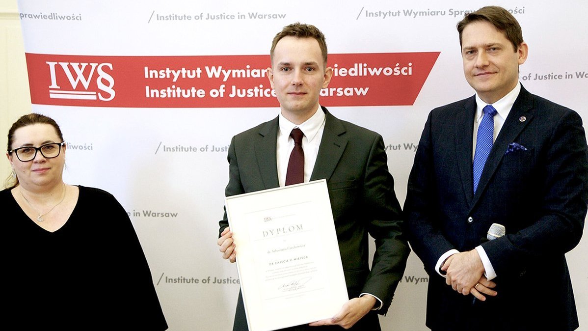 Trzy osoby na tle ścianki konferencyjnej.
