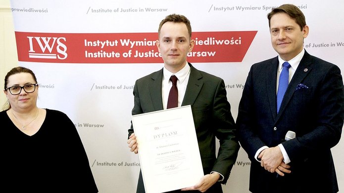 Trzy osoby na tle ścianki konferencyjnej.
