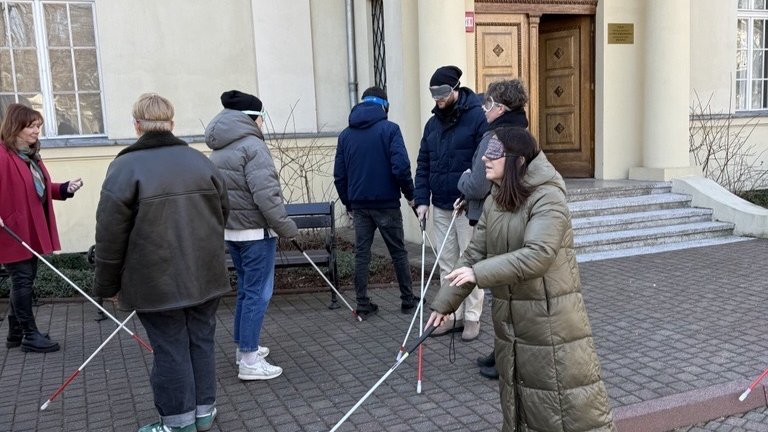 grupa ludzi z zasłoniętymi oczami, poruszająca się przy użyciu białej laski 