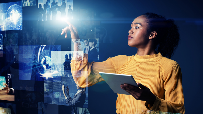 A young woman holding a tablet and pointing at images on a holographic screen