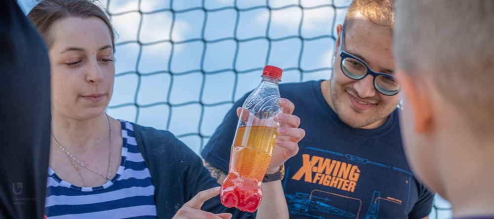 studenci pokazujący dzieciom butelkę z kolorowymi cieczami