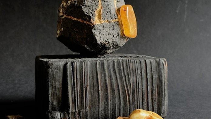 Zdjęcie przedstawia rzeźbę oraz bursztyny na czarnym podkładzie.